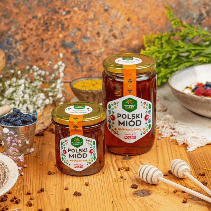 Dwa słoiki miodu wielokwiatowego polskiego - 400g i 900 g, stojące na drewnianym stole.